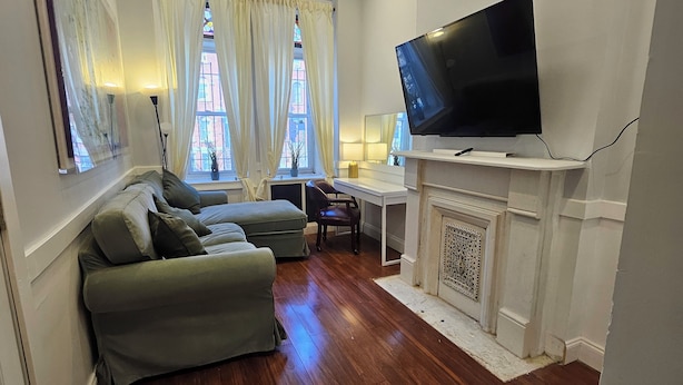 Een woonkamer met een bank, een televisie, een open haard en een raam met gordijnen.