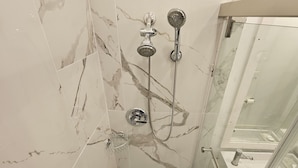 Douche met glazen deur, marmeren wanden en een zichtbare afvoer.