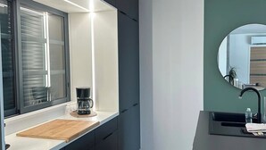 A modern kitchen with dark cabinetry, a white countertop, a coffee maker, and a round mirror above the sink. - Gîte Luna villa 6 persons with jacuzzi, children's playground and petanque area (Chaumont-sur-Loire)