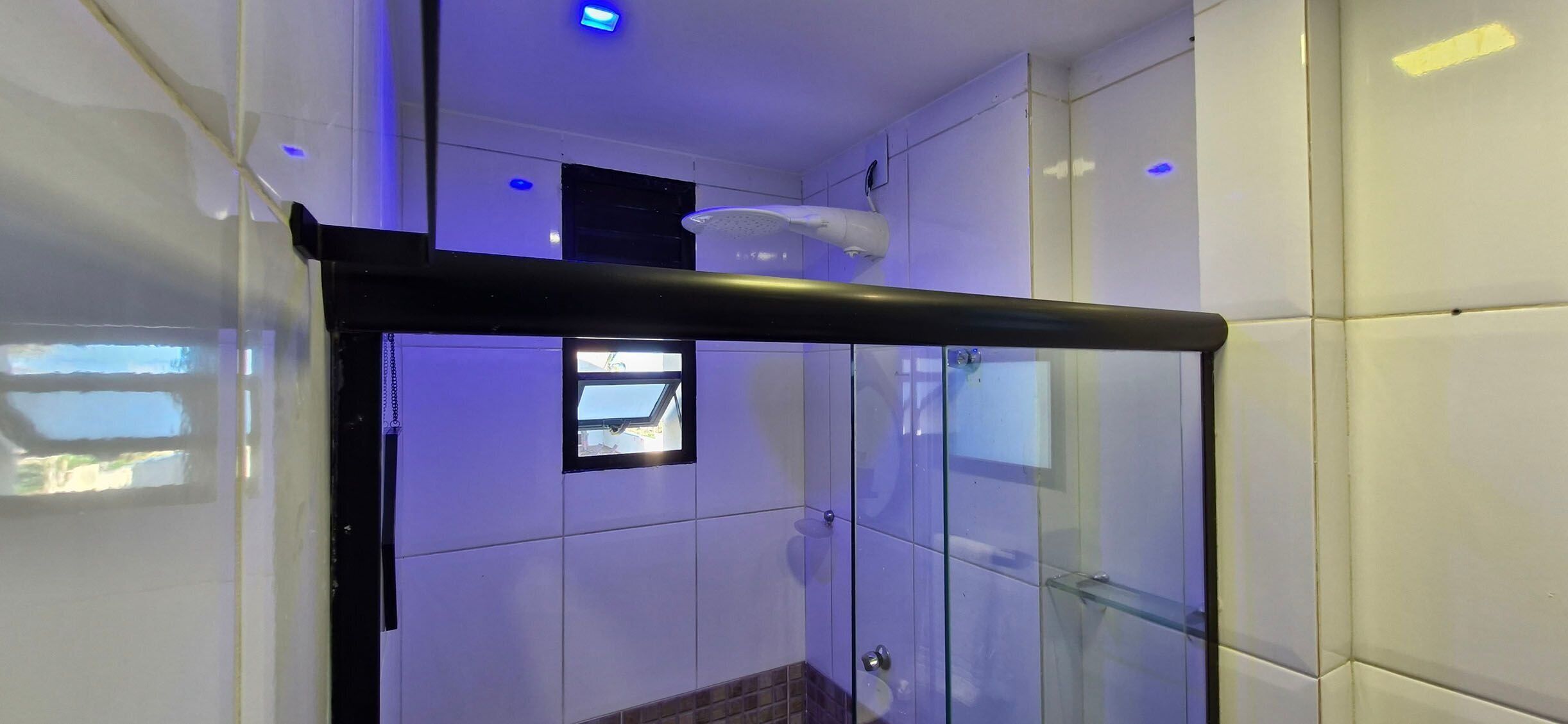 A modern bathroom with a glass shower enclosure, a ceiling fan, and a small window.