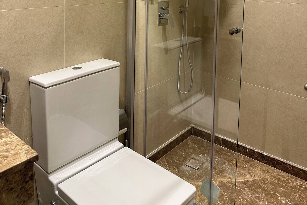 A modern bathroom with a glass-enclosed shower, a toilet, and a hand dryer.