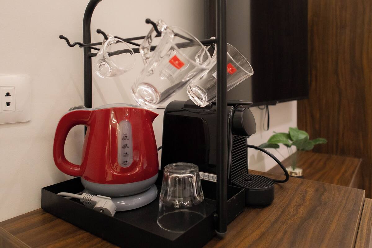 A modern kitchen area with a coffee maker, kettle, and glassware holder on a wooden countertop.