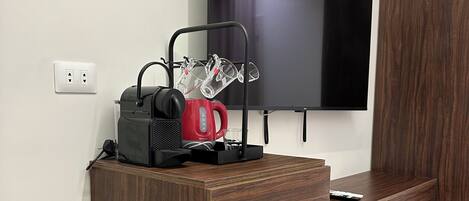 Una kitchenette compacta con refrigerador, cafetera y televisor montado en la pared.