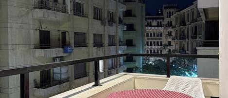 Un balcón con mesa y sillas, con vista a un edificio con varios balcones y ventanas.