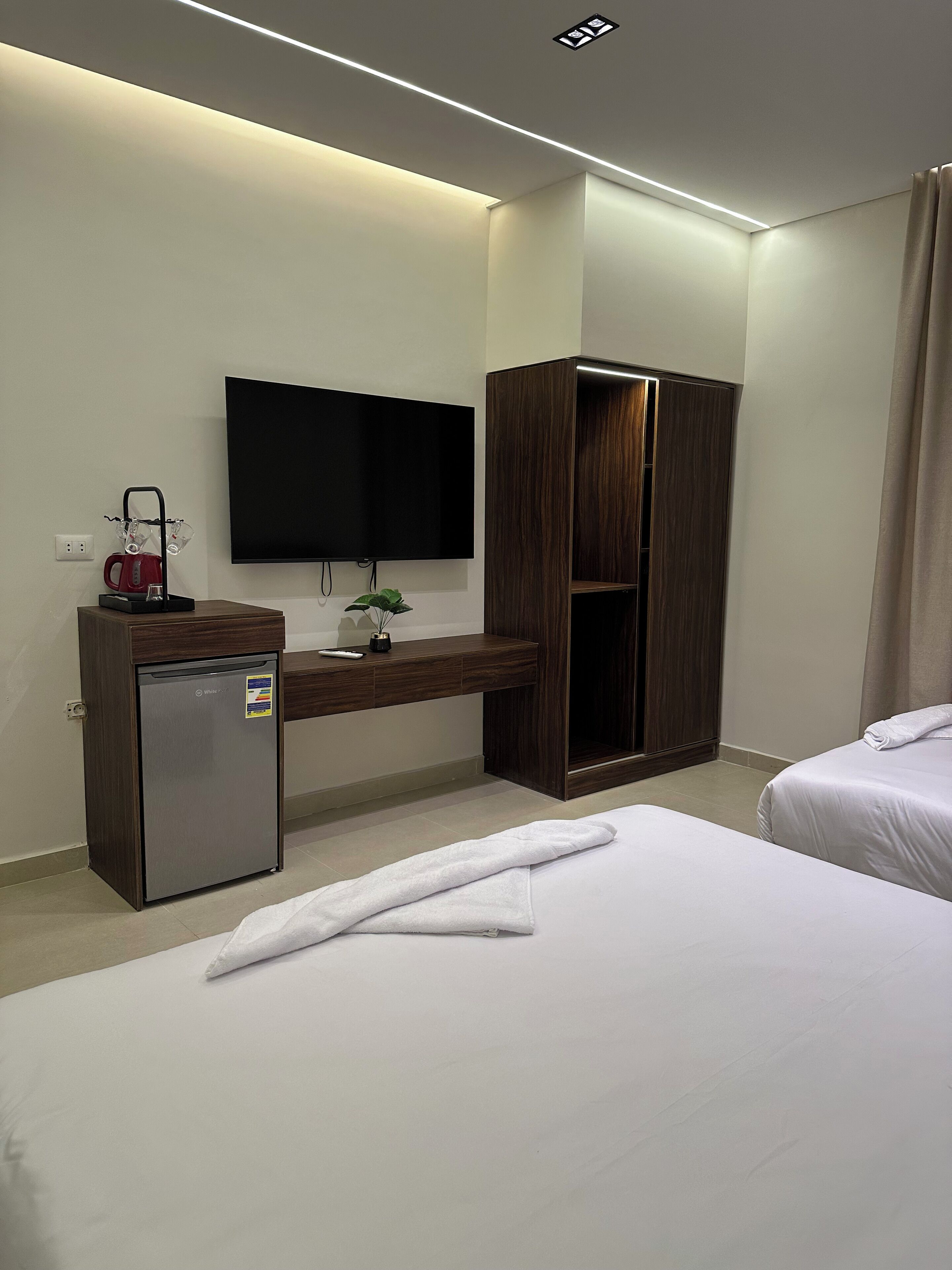 A hotel room with a bed, a desk with a TV, a minibar, and a wardrobe.