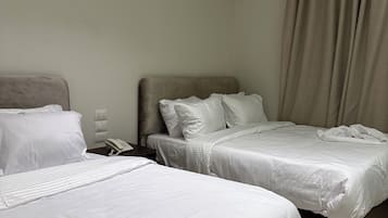 Twee eenpersoonsbedden met witte lakens, een bedtelefoon en een wandairconditioning.