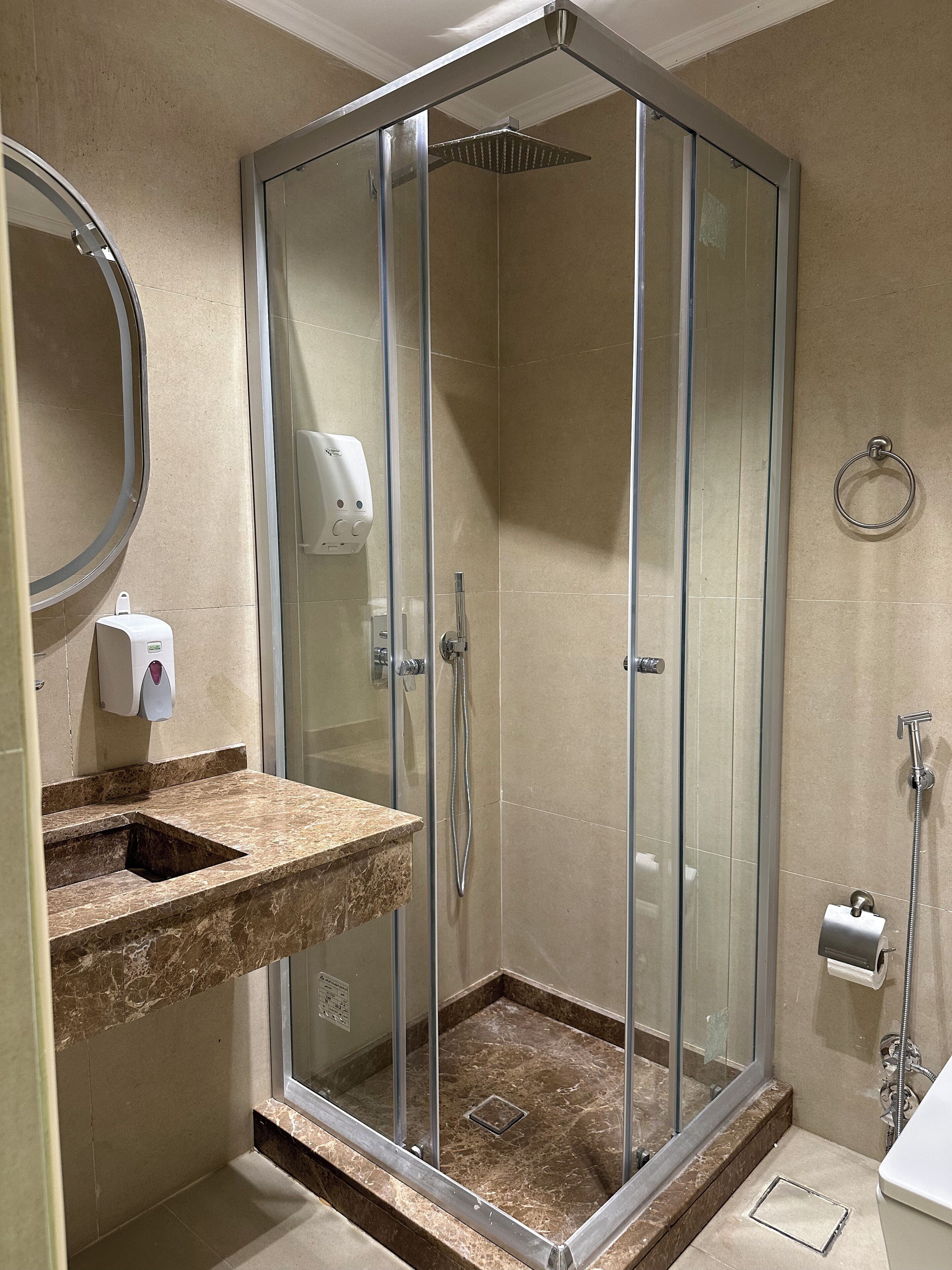 A modern bathroom with a glass-enclosed shower, a marble countertop, a hand soap dispenser, and a towel ring.
