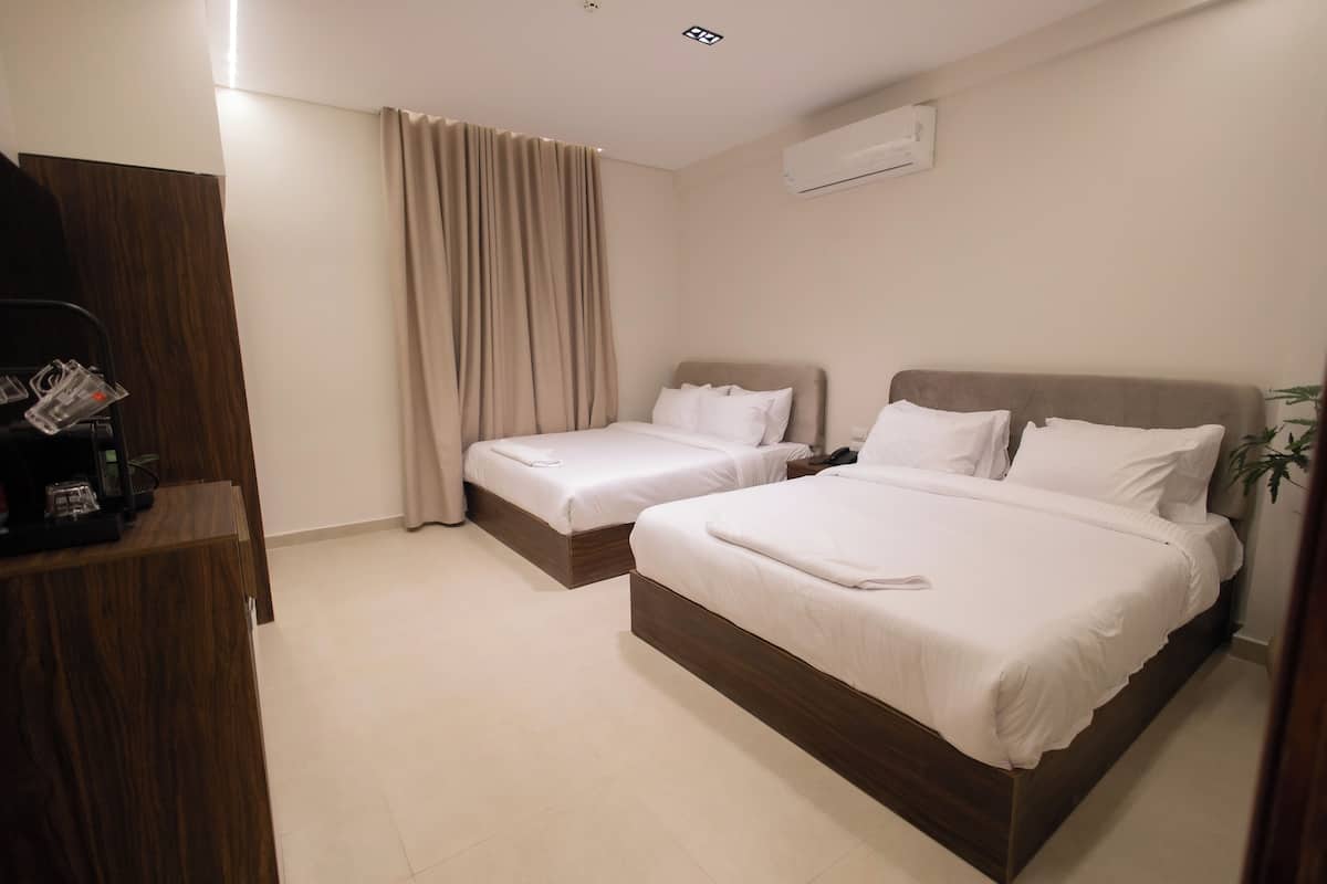 A hotel room with two beds, a wooden dresser, and a ceiling light.
