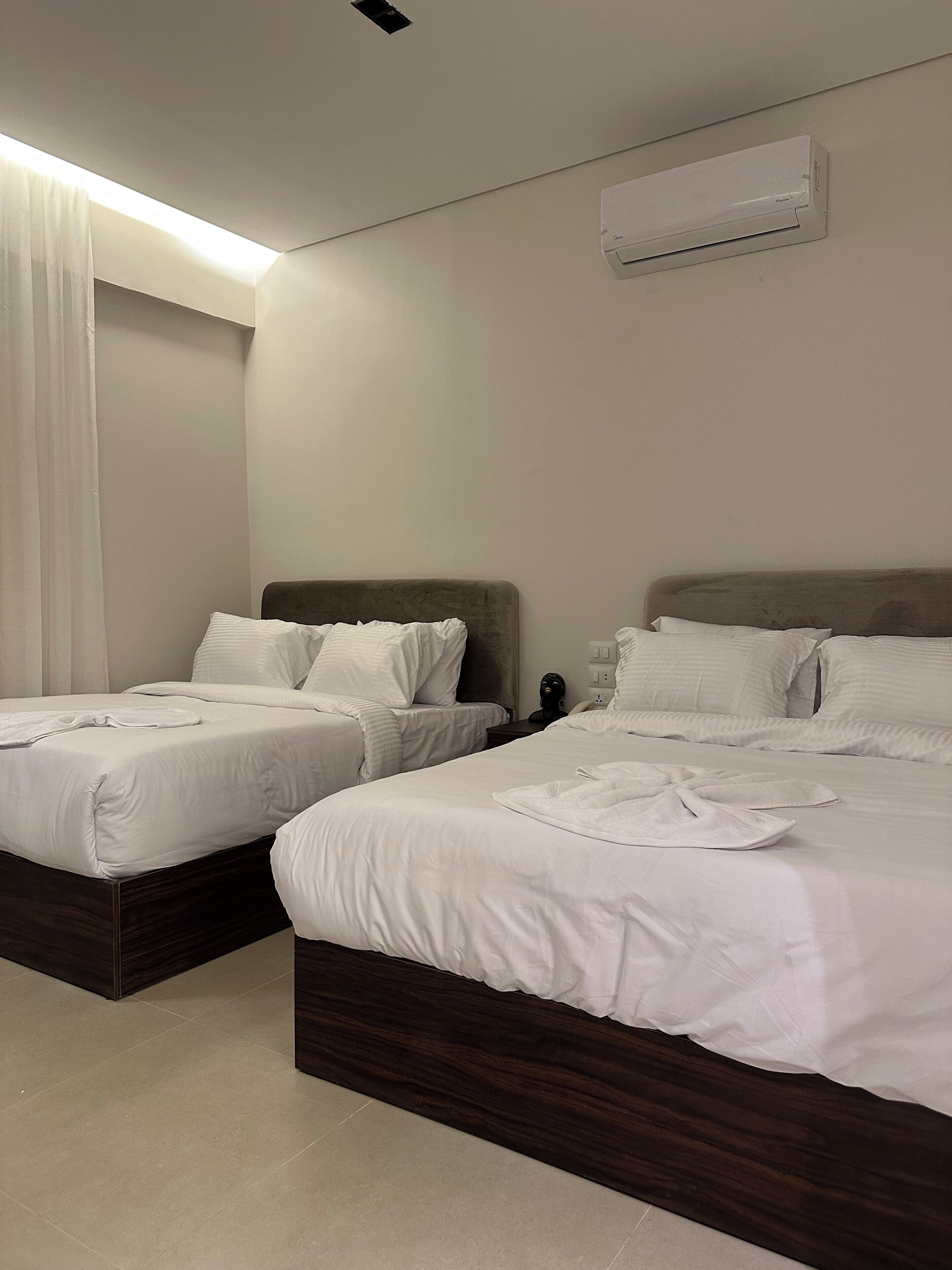 A hotel room with two beds, white linens, a dark wooden headboard, a ceiling light, and an air conditioning unit.