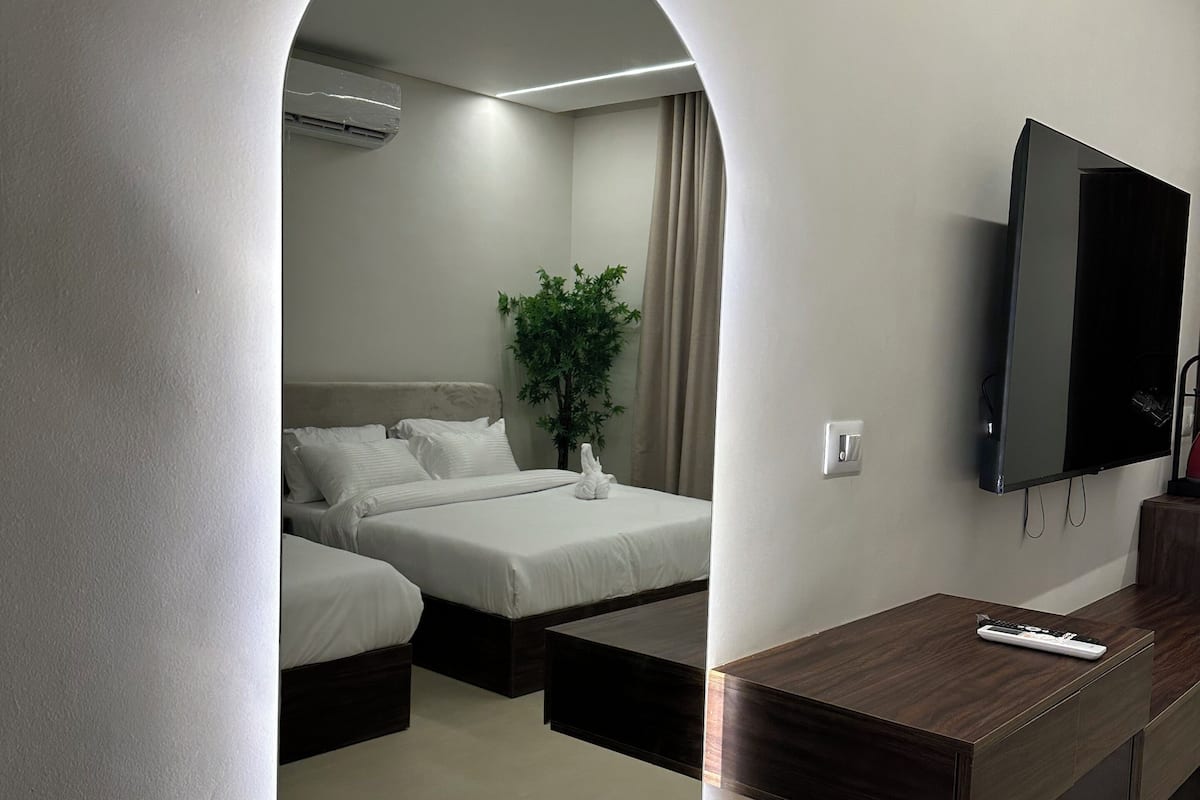 A modern hotel room with a large mirror, a flat-screen TV, a wooden desk, and a bed with two pillows.