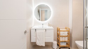 Ein modernes Badezimmer mit rundem Spiegel, weißem Waschbecken und einem Holzhandtuchhalter.