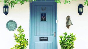 Eine blaue Tür mit kleinem Fenster, einer Glocke und zwei Wandleuchtern.