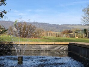A water feature with a fountain in a landscaped area with a view of hills and a fence in the background. - 5-bed Home - Sleeps 12, Pool, Garden & Play Area (Taunton)