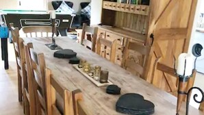 Ett långt matbord i trä med stolar, ett bricka med glas och en flaska, och ett svart föremål på bordet.