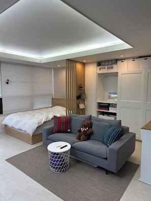 Un dormitorio moderno con cama, sofá gris y un oso de peluche.