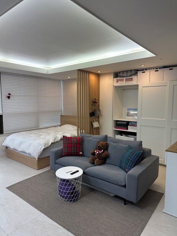 A modern bedroom with a bed, grey sofa, and a teddy bear.