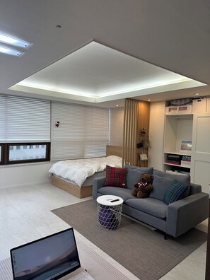 A modern bedroom with a bed, a grey sofa, a small round table, and a laptop on the floor.