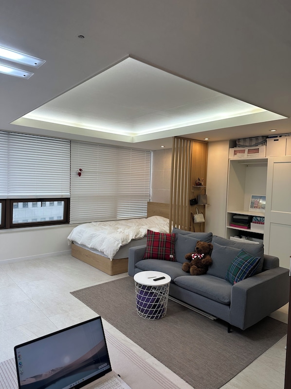 A modern bedroom with a bed, a grey sofa, a small round table, and a laptop on the floor.