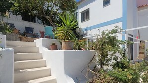 A white building with blue trim, a staircase leading to a door, and various potted plants. - 2-BR House with garden in fishing village Ferragudo, by the river and the ocean. (Ferragudo)