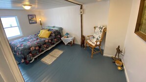 A bedroom with a bed, a chair, a small table, and a window.