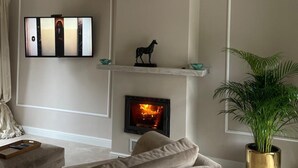 Een woonkamer met een open haard, een aan de muur bevestigde televisie, een bank en een kroonluchter.