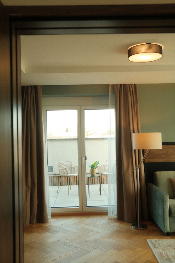 A room with a sliding glass door leading to an outdoor area, a floor lamp, and a sofa. - UNICO Boutique Hotel (Hochheim am Main)
