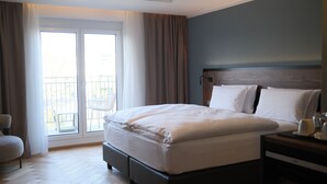 A hotel room with a large bed, a wooden headboard, a small bedside table, and a view of a balcony with outdoor furniture. - UNICO Boutique Hotel (Hochheim am Main)