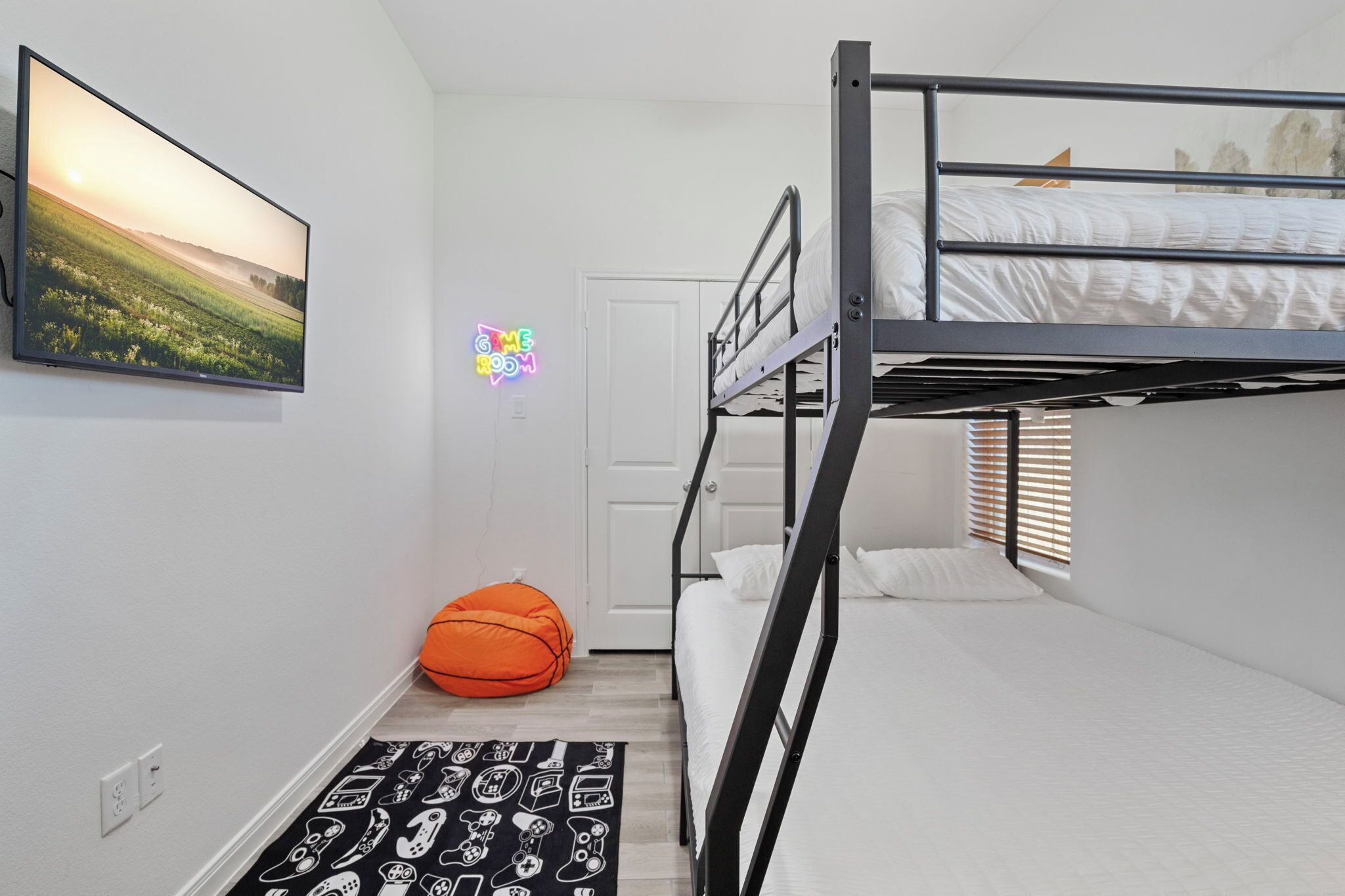 Une chambre avec un lit superposé, un téléviseur fixé au mur, une porte et un fauteuil en forme de sac de haricots.