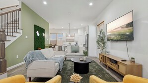 Ein modernes Wohnzimmer mit einer Couch, gelben Sesseln, einem Couchtisch und einem an der Wand montierten Fernseher.