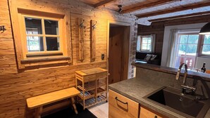 Interior de una cabaña de madera con área de cocina que incluye un lavamanos, encimera y armarios de madera.