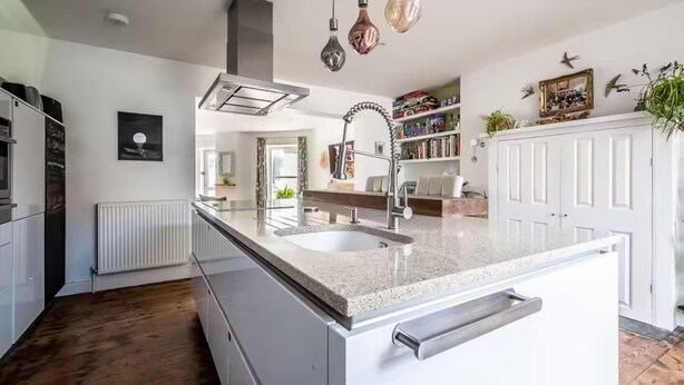Une cuisine moderne dotée d’un îlot central, d’appareils électroménagers en acier inoxydable et de luminaires suspendus.