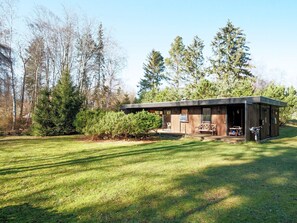 Une cabane moderne dotée d’un porche abrité, entourée d’une pelouse bien entretenue et d’arbres denses.