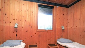 Een houten kamer met twee bedden, een raam en twee wandlampen.