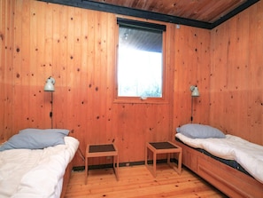 Une chambre de style cabane en bois, avec deux lits, une fenêtre et deux lampes fixées au mur.