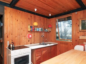 Une cuisine de taille réduite avec des murs en bois, une cuisinière, un évier et une fenêtre donnant sur les arbres.