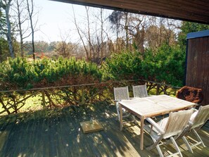 Une terrasse en bois avec une table et des chaises, entourée de verdure et d’arbres.