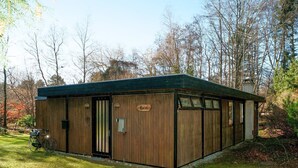Een houten hutje met een bord waarop 'Cottage' staat, gelegen in een bebost gebied.
