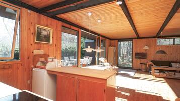 Interior de madera con cocina, comedor y un amplio ventanal que proporciona luz natural.
