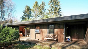 Een moderne houten cabin met een terras, een overdekte zithoek en een groot raam met uitzicht op het omliggende bos.
