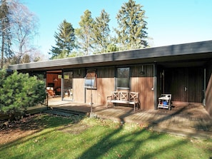 Een moderne houten cabin met een terras, een overdekte zithoek en een groot raam met uitzicht op het omliggende bos.