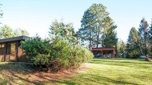 Een moderne cabin met een groot raam, omgeven door een verzorgd gazon en hoge bomen.