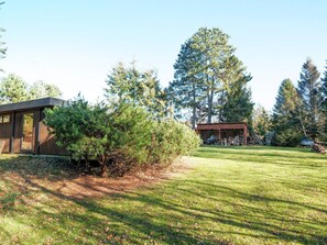 Une cabane moderne dotée d’une grande fenêtre, entourée d’une pelouse bien entretenue et de grands arbres.