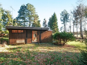 Une petite cabane au revêtement extérieur en bois, avec un banc à l’extérieur et une vue dégagée sur la forêt environnante.