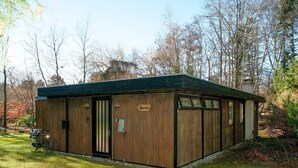 Une cabane en bois avec une pancarte indiquant « Cottage », un vélo garé à l’extérieur et une zone herbeuse avec des arbres en arrière-plan.