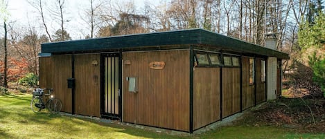 A wooden cabin with a sign reading 'Cottage,' a bicycle parked outside, and a grassy area with trees in the background.