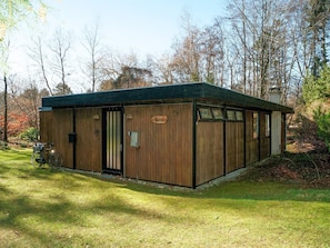 Une cabane en bois avec une pancarte indiquant « Cottage », un vélo garé à l’extérieur et une zone herbeuse avec des arbres en arrière-plan.