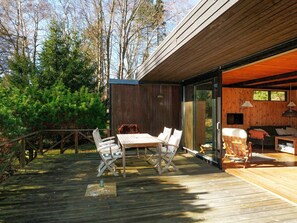 Een houten terras met een tafel en stoelen, een bank en een televisie in een modern interieur.
