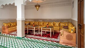 A room with a patterned floor, a sofa set with patterned cushions, a coffee table, and a hanging light fixture. - Riad Ilyan & Spa  (Marrakech)