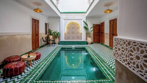A swimming pool with a geometric patterned floor, a central fountain, and a view of a courtyard through an arched window. - Riad Ilyan & Spa  (Marrakech)