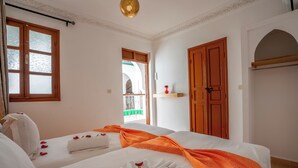 A hotel room with two beds, a wooden door, a window with frosted glass, and a balcony visible through the window. - Riad Ilyan & Spa  (Marrakech)